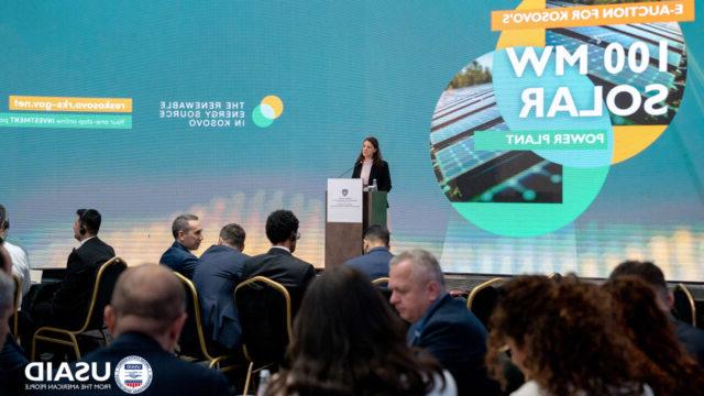 A person speaking at a podium at Kosovo’s first-ever renewable energy auction, which competitively solicited 100 megawatts of solar energy